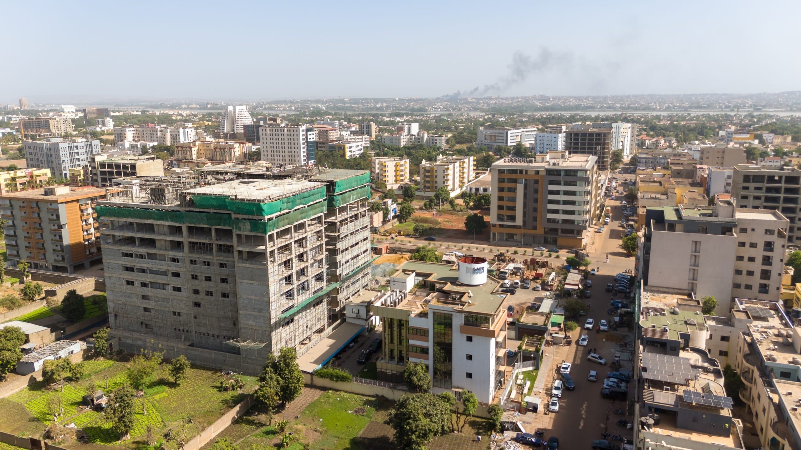 Vue aérienne du centre de Bamako : une grande tour de béton en construction au milieu d’immeubles de moyenne hauteur, le fleuve et les collines à l’horizon. — API-Mali